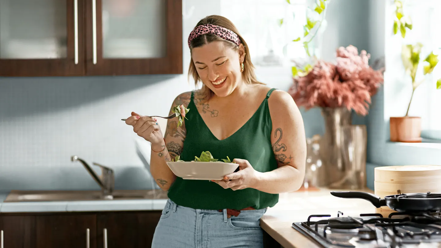 woman enjoying her salad standing in her kitchen