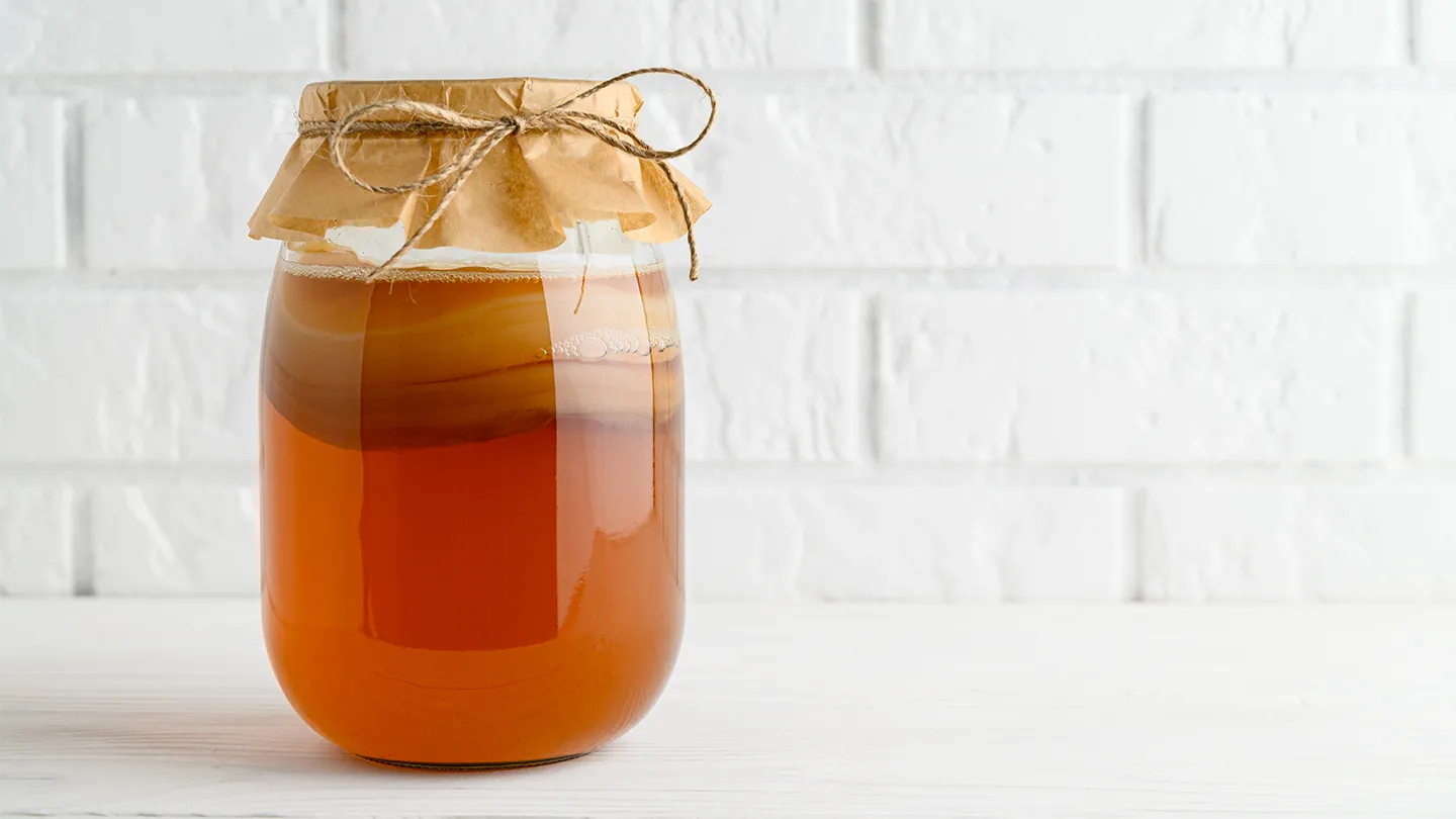 Homemade fermented kombucha tea in a glass jar on a background of a white brick wall