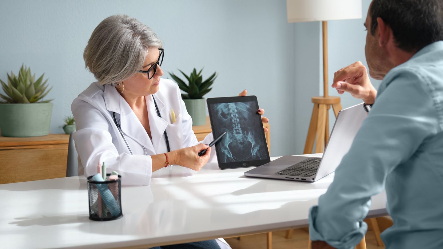 woman doctor showing male patient xray of pelvic area on a tablet in her office