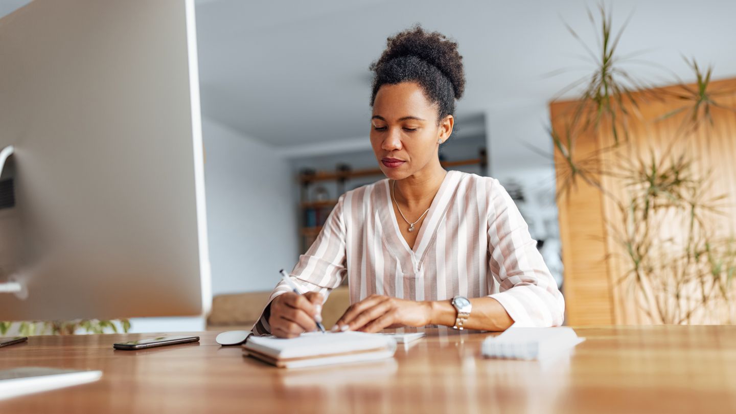 mature Black woman sitting at her desk at home writing down questions