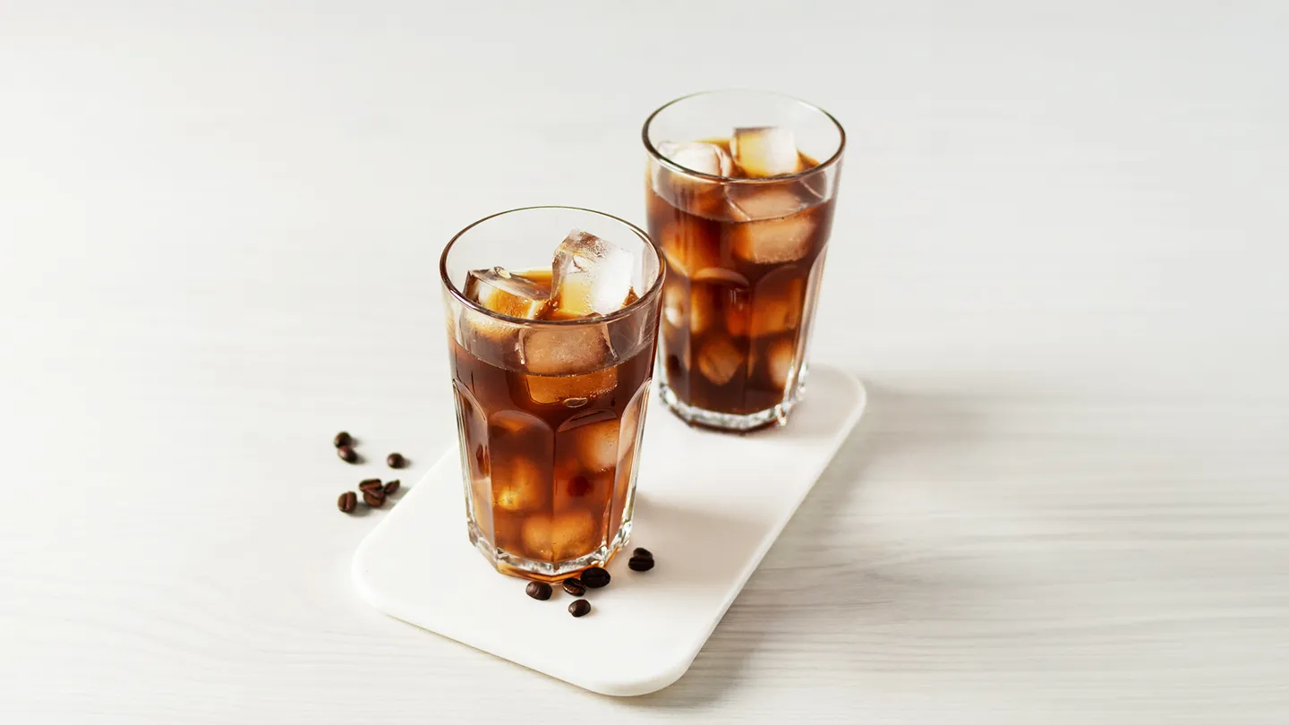 two glasses of black iced coffee cold brew with coffee beans on marble slab in kitchen