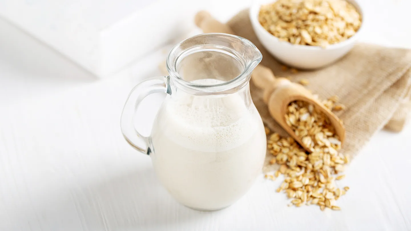 large pitcher of oat milk and bowl and wooden spoon full of oats