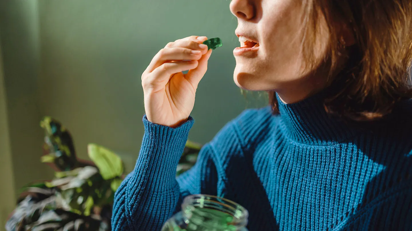 woman in a blue turtleneck taking a sea moss gummy
