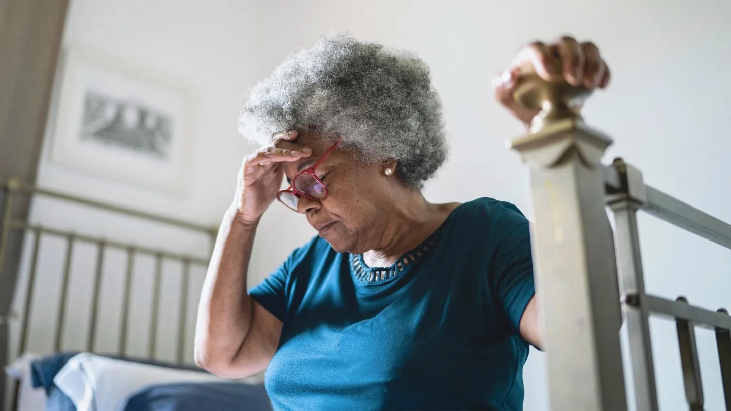 sleep deprived senior woman sitting on bed not feeling well
