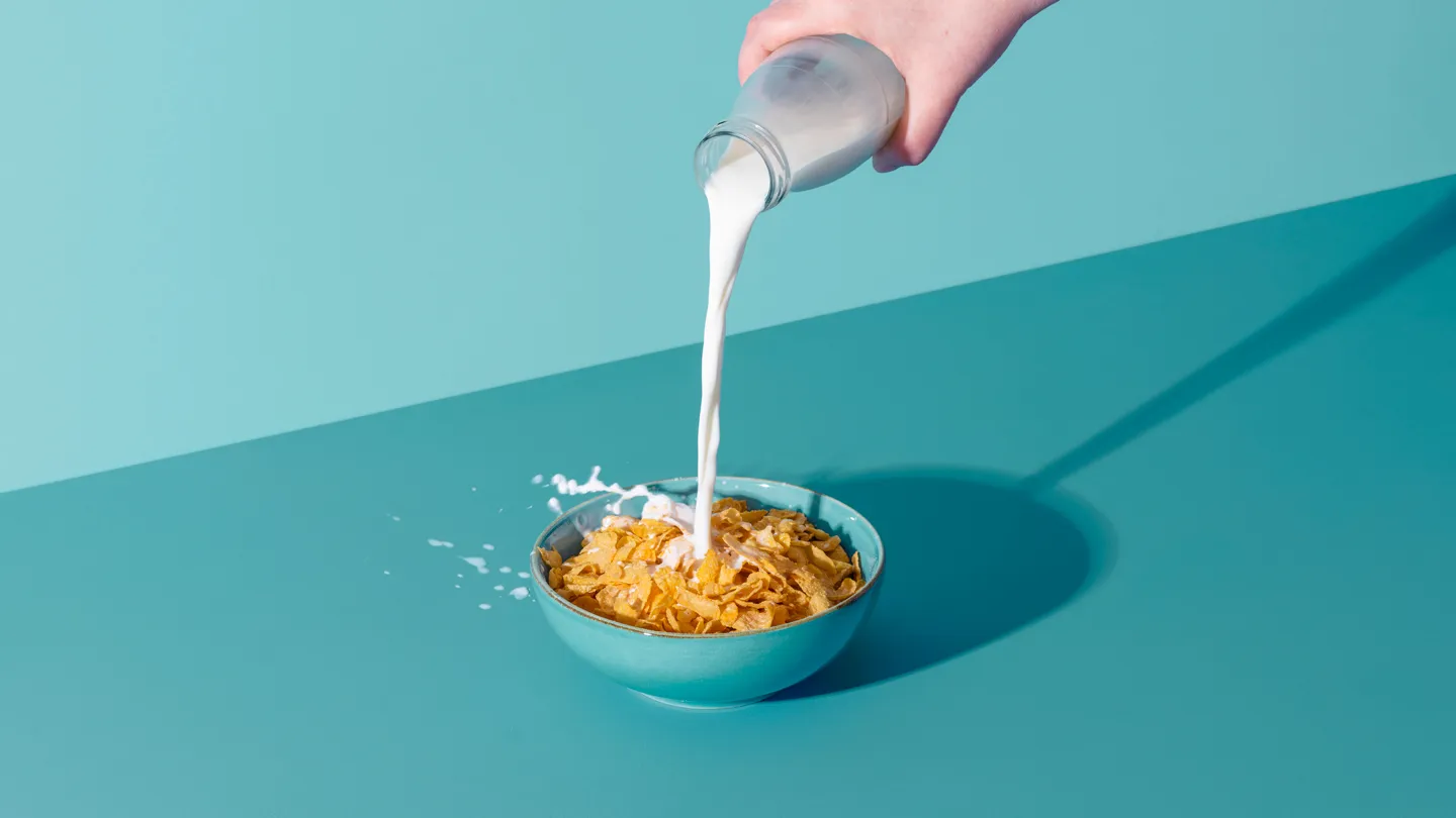 hand pouring milk into cereal bowl