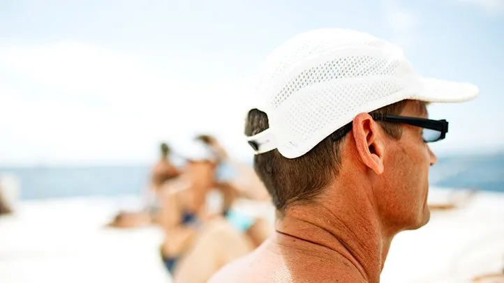 A man on the beach uses a baseball cap to prevent skin cancer.