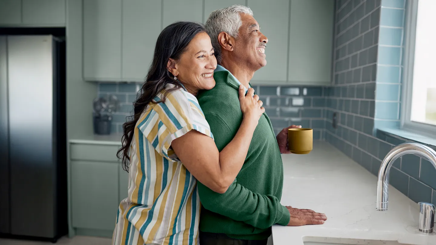 mature hispanic couple embracing looking out the kitchen window
