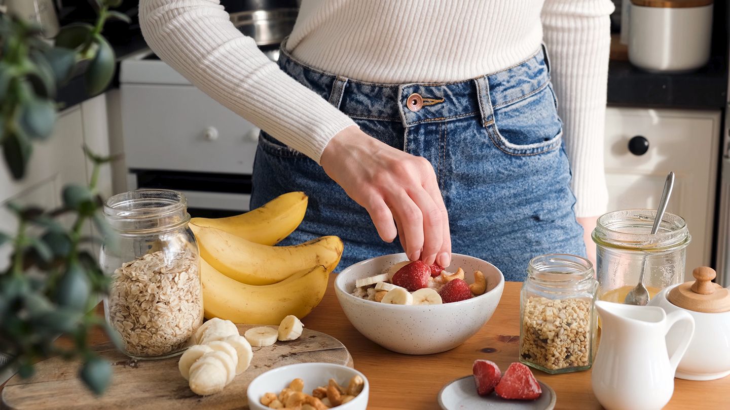 woman jeans putting fruit strawberries on oatmeal