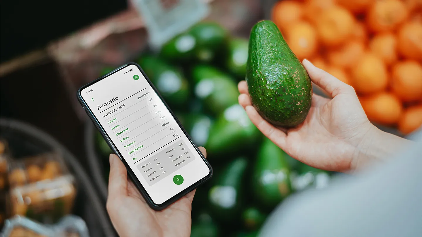 woman holding an avocado, using health and fitness tracker app on smartphone to check the nutrition facts and Macronutrients