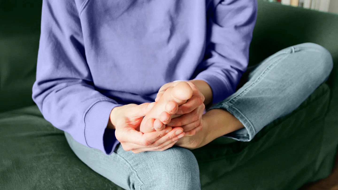woman holding her foot in pain or numbness sitting on the couch
