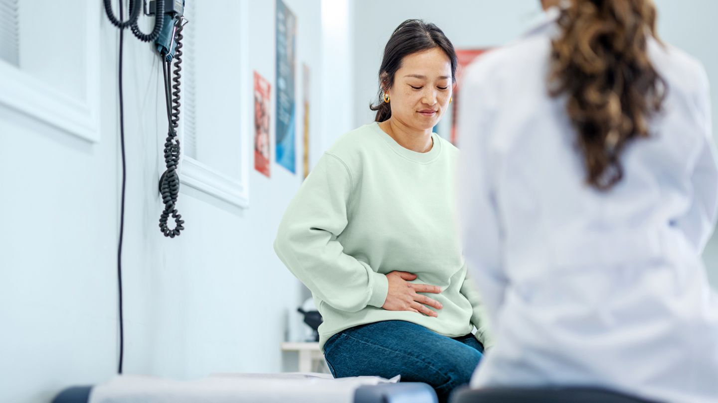 young woman holding her abdomen in pain at doctor's office