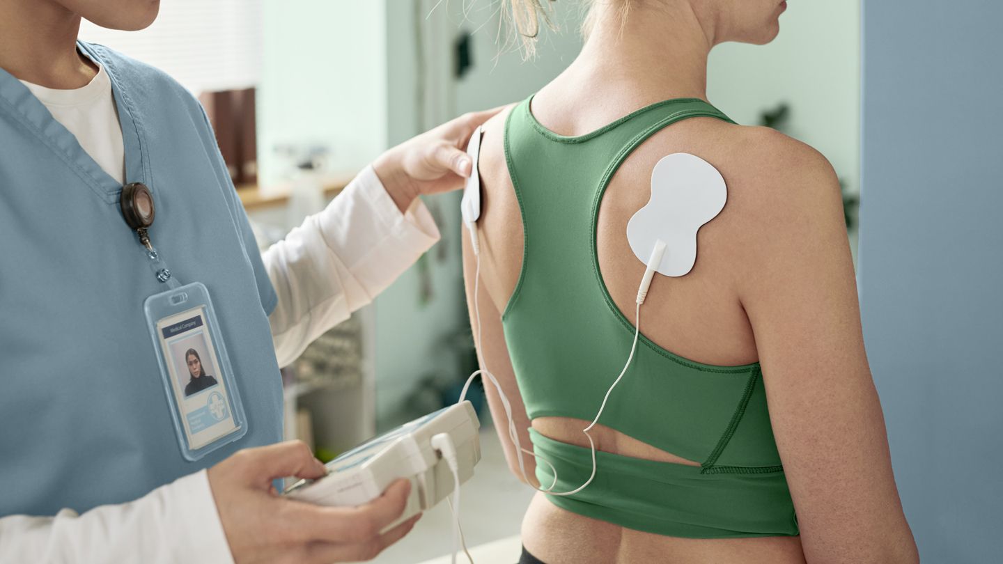 female patient receiving Transcutaneous Electrical Nerve Stimulation on her shoulder blades in phyisical therapy office
