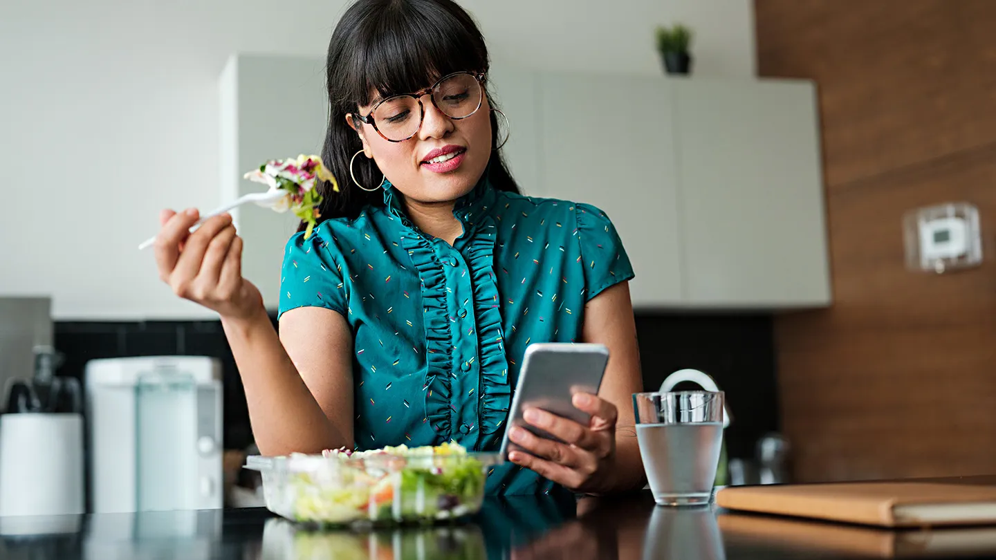 young hispanic latin woman eating salad looking at phone