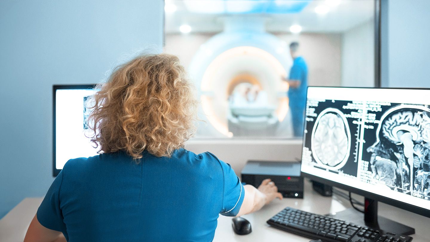 female radiologist in MRI scanning procedure control room looking at mri brain scan of patient in mri machine