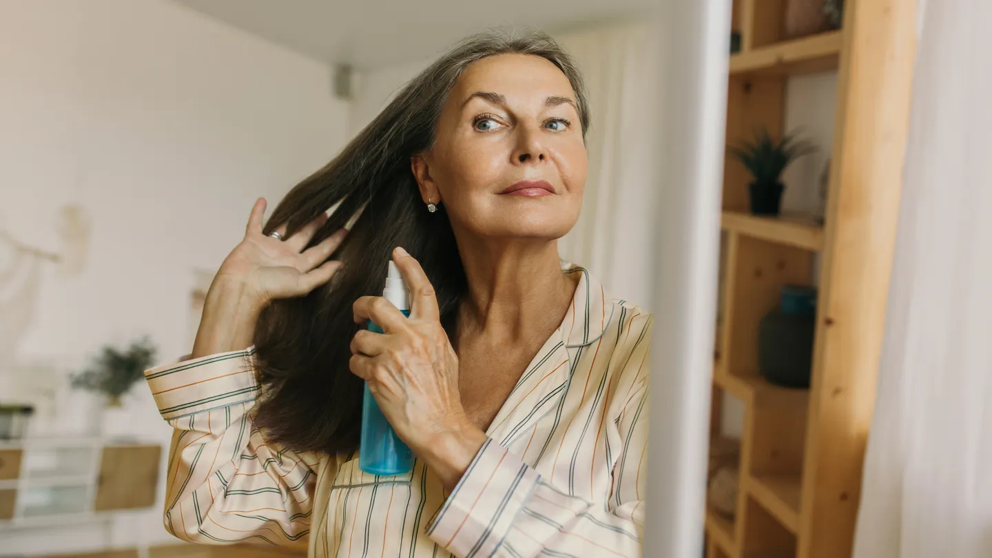 mature woman spraying product on her hair