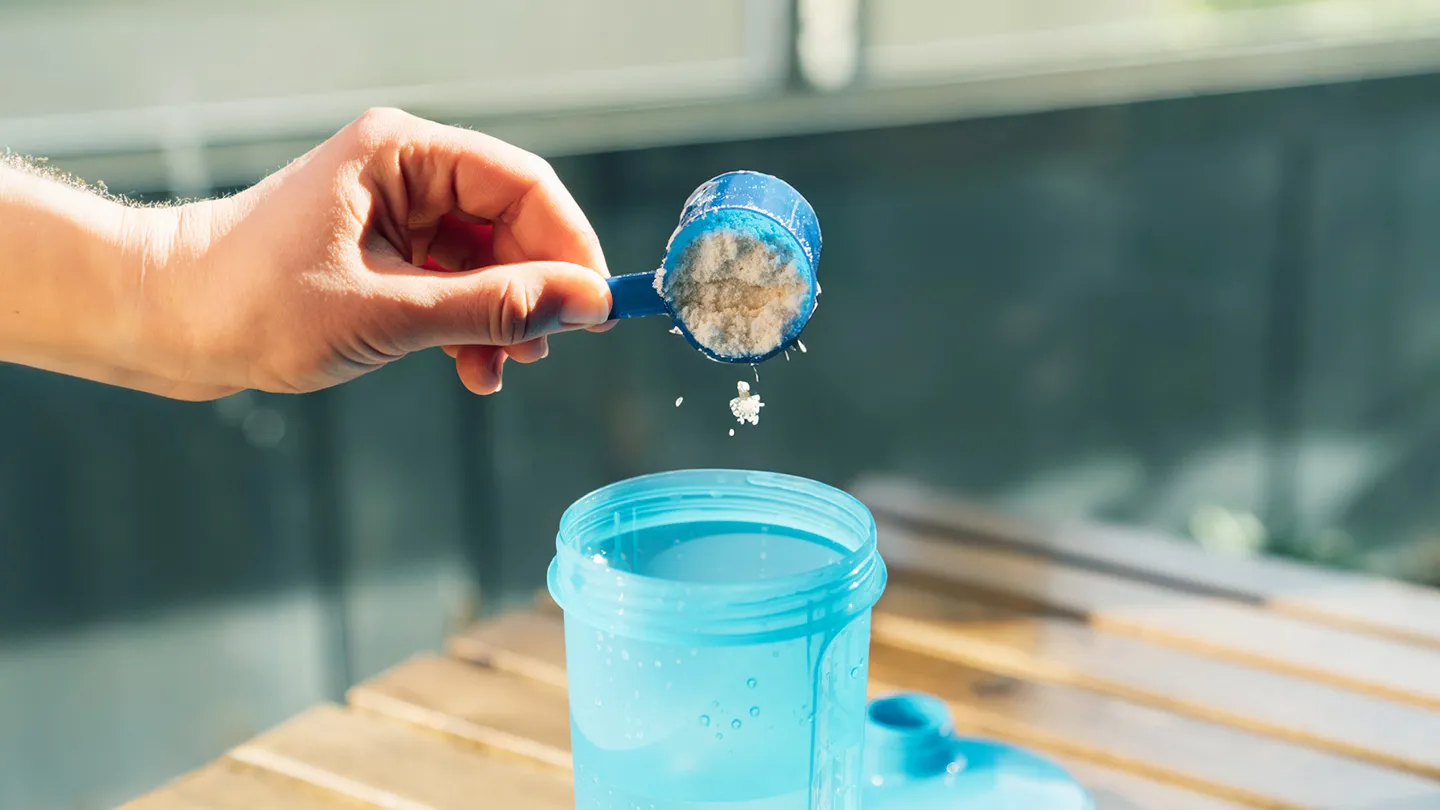 hand adding workout supplement powder to protein shaker bottle in kitchen