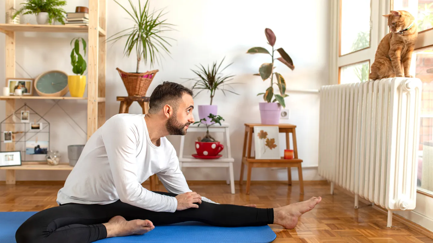 man practicing yoga looking at cat